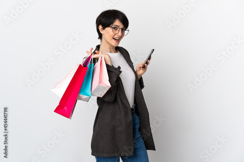 Woman with short hair isolated on white background holding shopping bags and writing a message with her cell phone to a friend