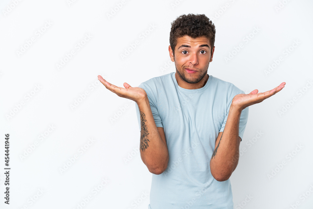 Young handsome Brazilian man isolated on white background having doubts while raising hands Young handsome Brazilian man isolated on white background having doubts while raising hands