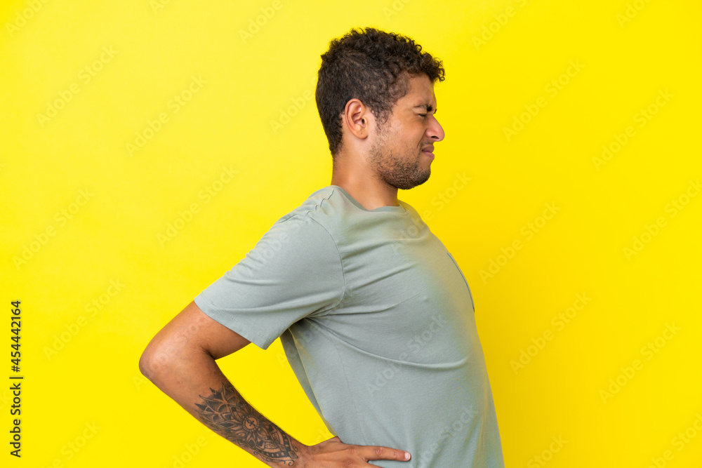 Young handsome Brazilian man isolated on yellow background suffering from backache for having made an effort Young handsome Brazilian man isolated on yellow background suffering from backache for having made an effort