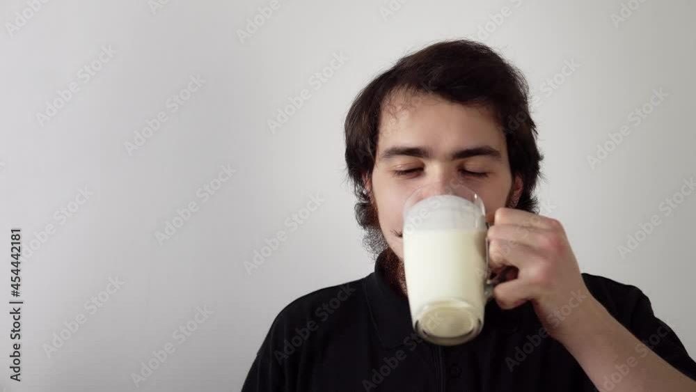 Isolated portrait of young bearded man drinking kefir from the glass and smiling on white background. A caucasian male person is consuming yogurt and enjoy it. The healthy lifestyle and dairy products Isolated portrait of young bearded man drinking kefir from the glass and smiling on white background. A caucasian male person is consuming yogurt and enjoy it. The healthy lifestyle and dairy products