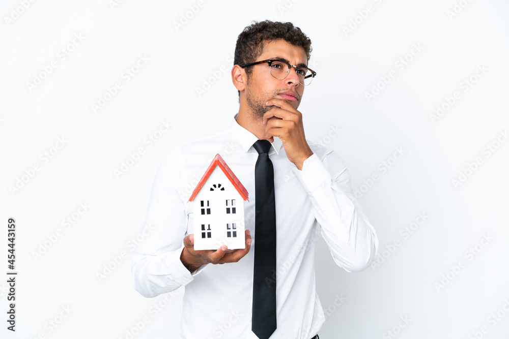 Young business Brazilian man holding a house toy isolated on white background and looking up Young business Brazilian man holding a house toy isolated on white background and looking up