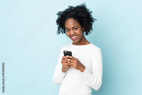 Young African American woman isolated on blue background sending a message with the mobile