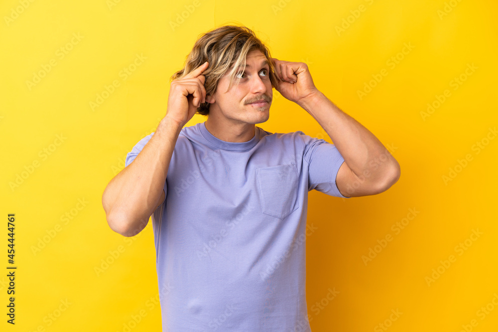 Handsome blonde man isolated on yellow background having doubts and thinking Handsome blonde man isolated on yellow background having doubts and thinking