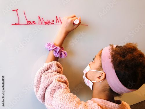 Young girl wearing a mask writing on a whiteboard photo