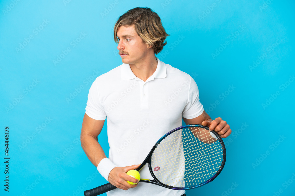 Young blonde man isolated on blue background playing tennis