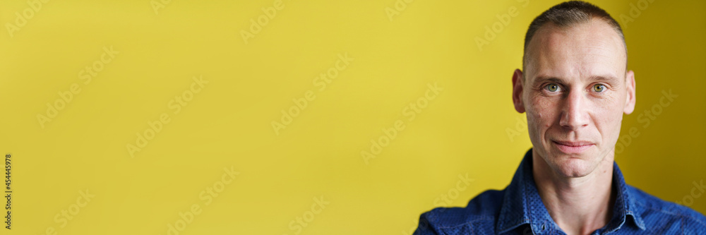 Obraz premium Front view close up portrait of male adult caucasian man with short blonde hair and green eyes in front of yellow background looking to the camera smiling with copy space