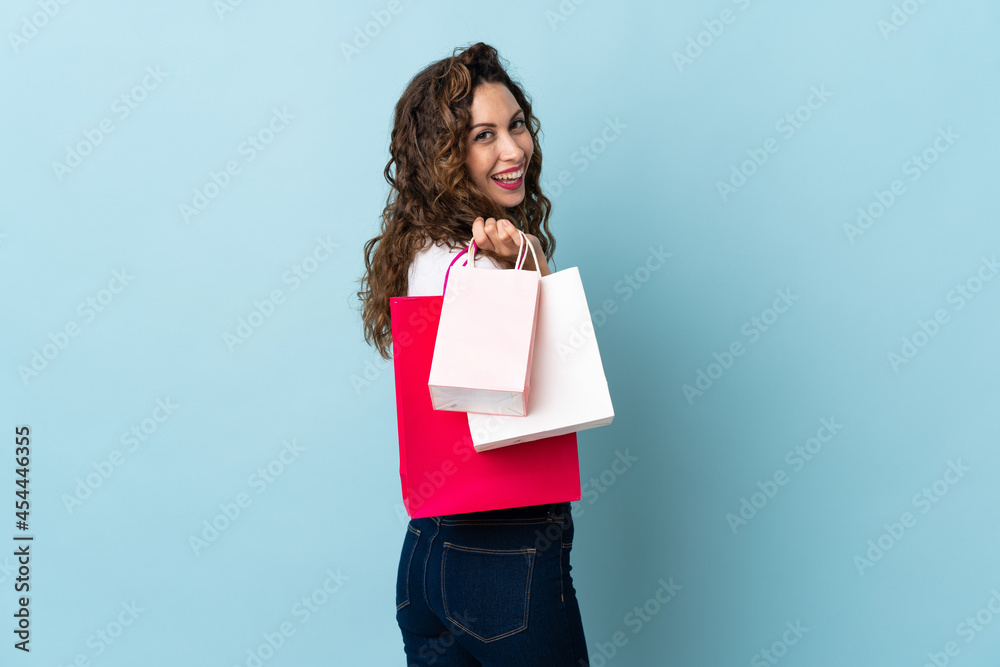 Fototapeta premium Young caucasian woman isolated on blue background holding shopping bags and smiling