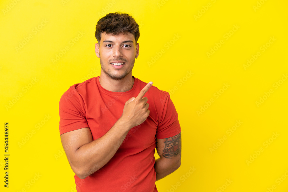 Young caucasian handsome man isolated on yellow background pointing to the side to present a product Young caucasian handsome man isolated on yellow background pointing to the side to present a product