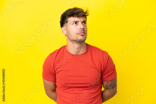 Young caucasian handsome man isolated on yellow background and looking up
