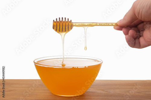 fresh floral honey dripping from a spoon into a transparent plate on a white background. organic vitamin health food
