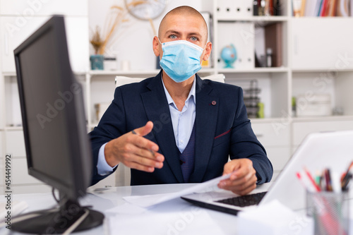 Young man in medical mask with hand extended to handshake in office