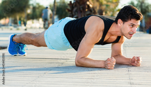 Strong sporty cheerful positive man doing press exercises holding plank outdoors © JackF