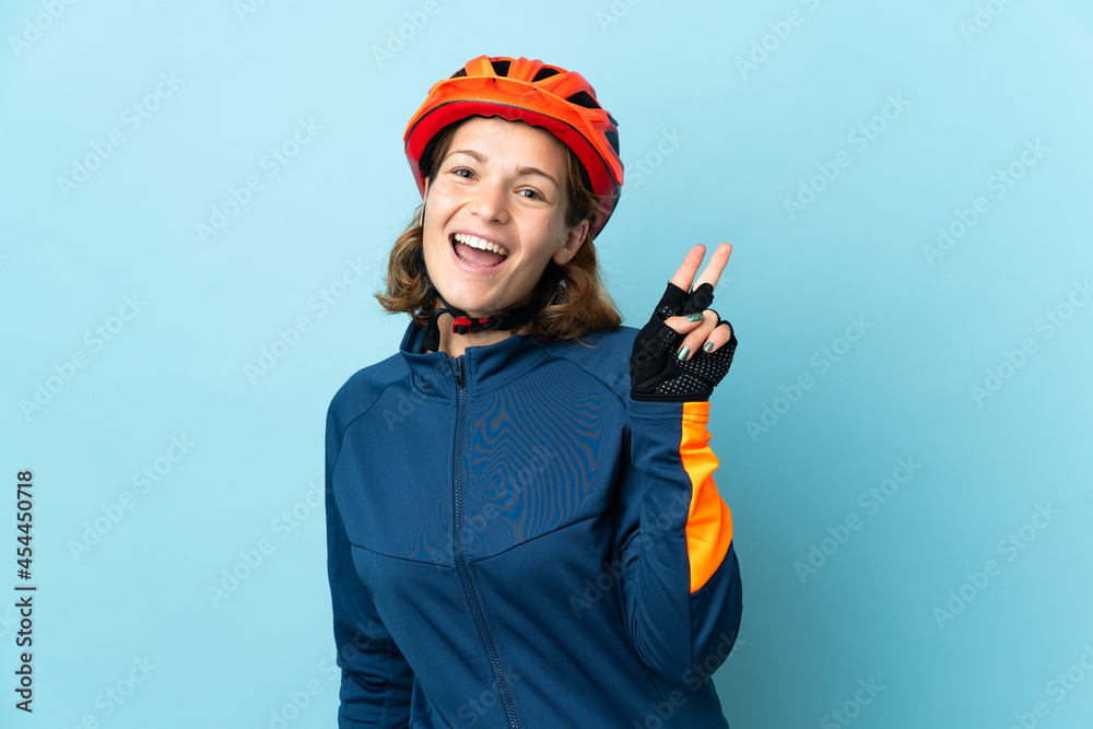 Young cyclist woman isolated on blue background smiling and showing victory sign Young cyclist woman isolated on blue background smiling and showing victory sign