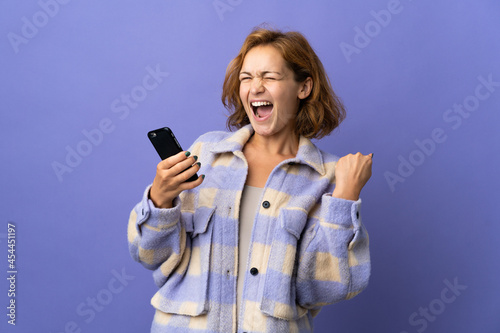 Young Georgian woman isolated on purple background with phone in victory position