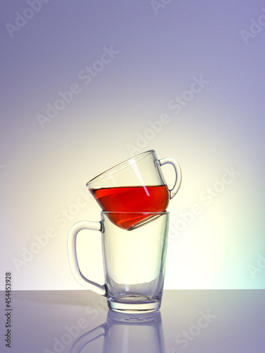 A clear glass mug filled with a red liquid, installed in another empty mug on a table with a matte finish in the rays of daylight lamps, a close-up, a colored background.