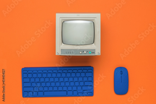 A gray monitor and a blue keyboard and mouse on an orange background. photo