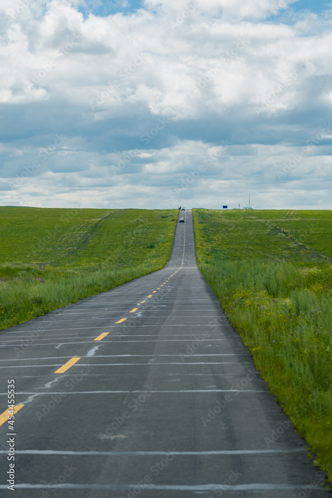 A road on green grassland during summer time.