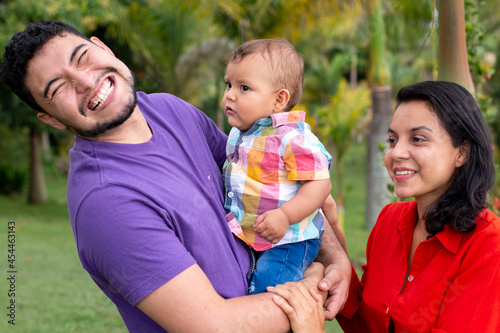 Smiling parents taking care of their baby in a beautiful park full of nature. latin family concept.