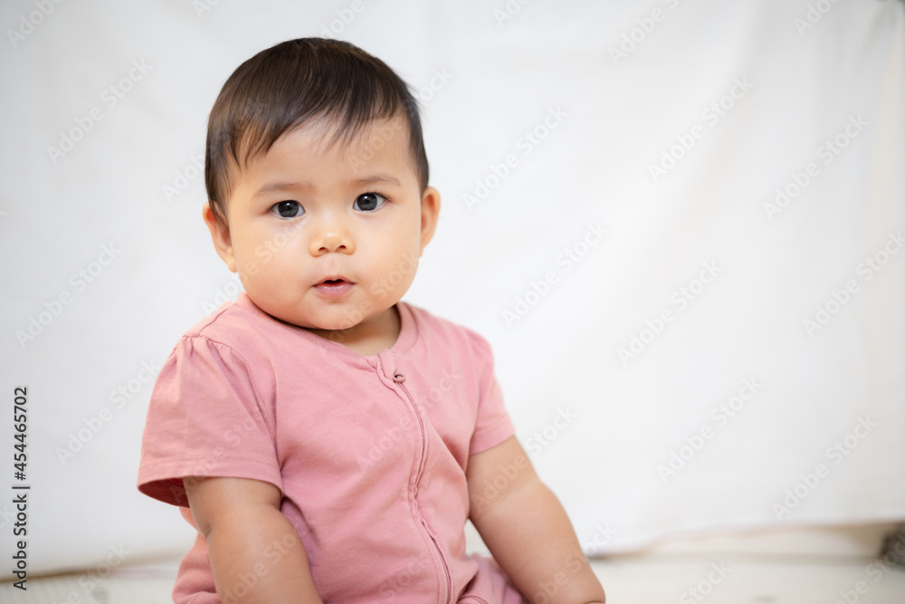 An Asian girl about 1 year old. Playing in the living room in the house. A cute baby wearing a pink dress Stay with parents in the house