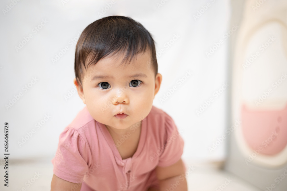 An Asian girl about 1 year old. Playing in the living room in the house. A cute baby wearing a pink dress Stay with parents in the house