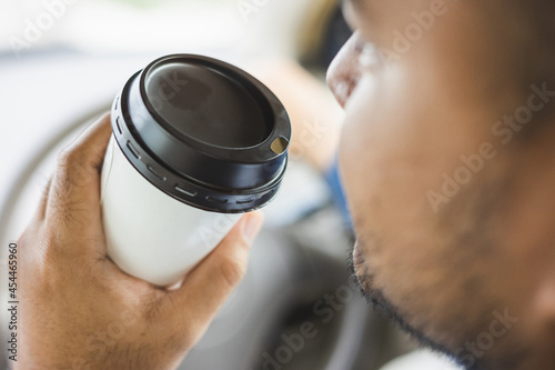 Young man drinking a cup of hot coffee while driving car to travel. Hands holding steering wheel.