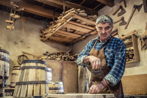Aged man with grey hair does carpentry job in an old workshop