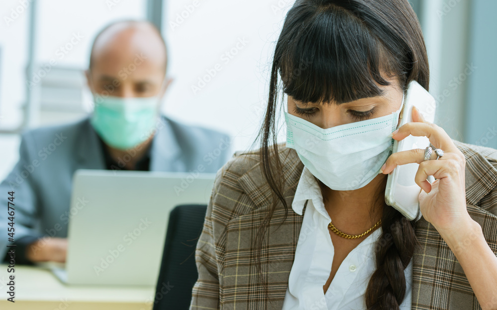 Smart Caucasian businesswoman wearing face mask protect virus, new normal, social distancing, talking on mobile phone with customer, working with intention in office with blur background of colleague. Smart Caucasian businesswoman wearing face mask protect virus, new normal, social distancing, talking on mobile phone with customer, working with intention in office with blur background of colleague.