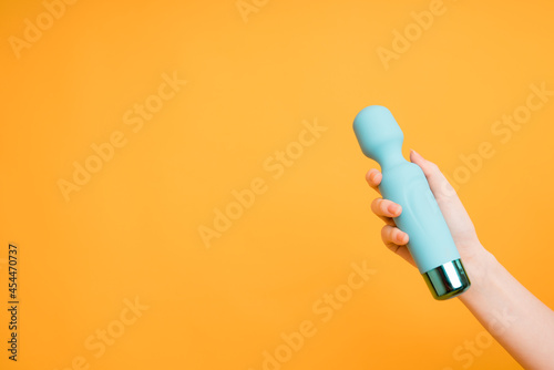 A blue vibrator for stimulating orgasm lies in a woman's hand on a yellow background.Useful for a sex shop