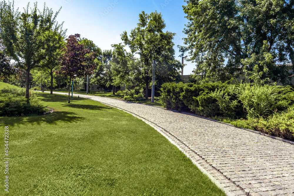 Green parkland with neatly mowed lawn and paved path on summer day