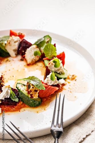 Close-up appetizing and fresh vegetable salad with beetroot, goat cheese, ripe tomato, cucumber, mustard leaves and spicy sauce. Delicious and healthy lunch. Serving restaurant dish. Food photography