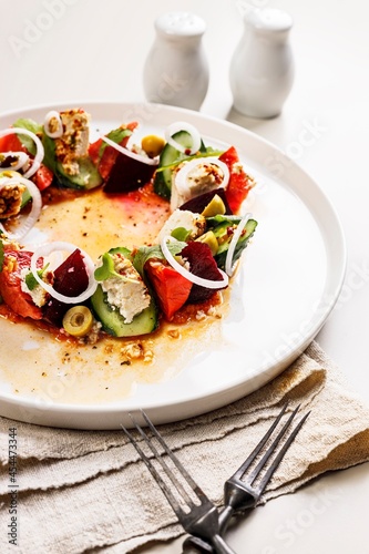 Close-up appetizing and fresh vegetable salad with beetroot, goat cheese, ripe tomato, cucumber, mustard leaves and spicy sauce. Delicious and healthy lunch. Serving restaurant dish. Vertical shot
