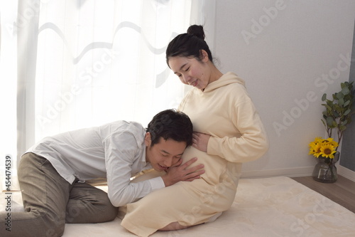 A young husband listens to fetal movements by listening to the large belly of a pregnant white-dressed young woman.