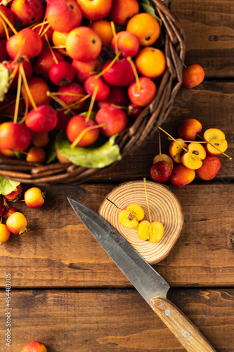 many small apples are lying in a wicker brown basket on a wooden table. several apples are cut in half with a knife with a wooden handle