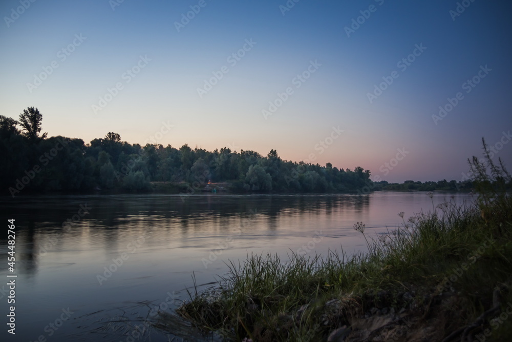 Forest and river at sunset. Deep blue-red sky at sunset near a c