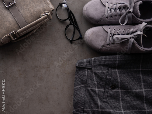 Gray sneakers, backpack, glasses and trousers in a cage on a dark background. Modern, youthful clothing. Women's set.