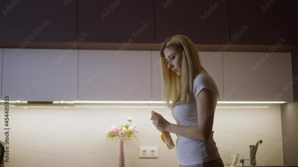 Young housewife in casual clothes wipes wet hands and throws towel finishing cleaning of elegant spacious kitchen at home side view slow motion Young housewife in casual clothes wipes wet hands and throws towel finishing cleaning of elegant spacious kitchen at home side view slow motion