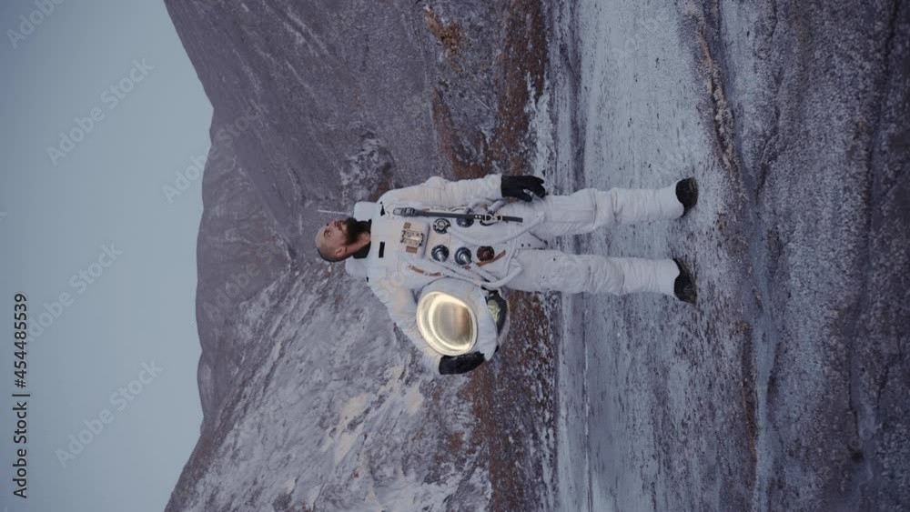 the astronaut stands with a helmet in his hand by the hills and looks to the side. discovery of a new planet. planet with a human-friendly atmosphere. vertical video
