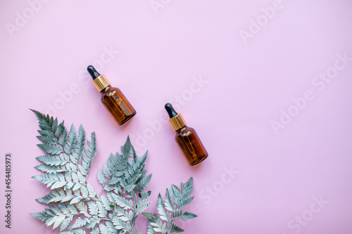 The layout of cosmetic serum bottles and decorative fern branch on pink background. High quality photo