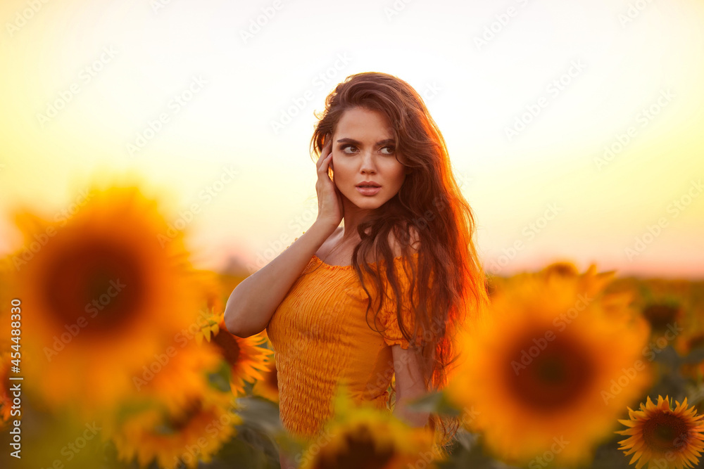 Beautiful young girl enjoying nature on the field of sunflowers at sunset. Summertime. Attractive brunette woman with long healthy hair.