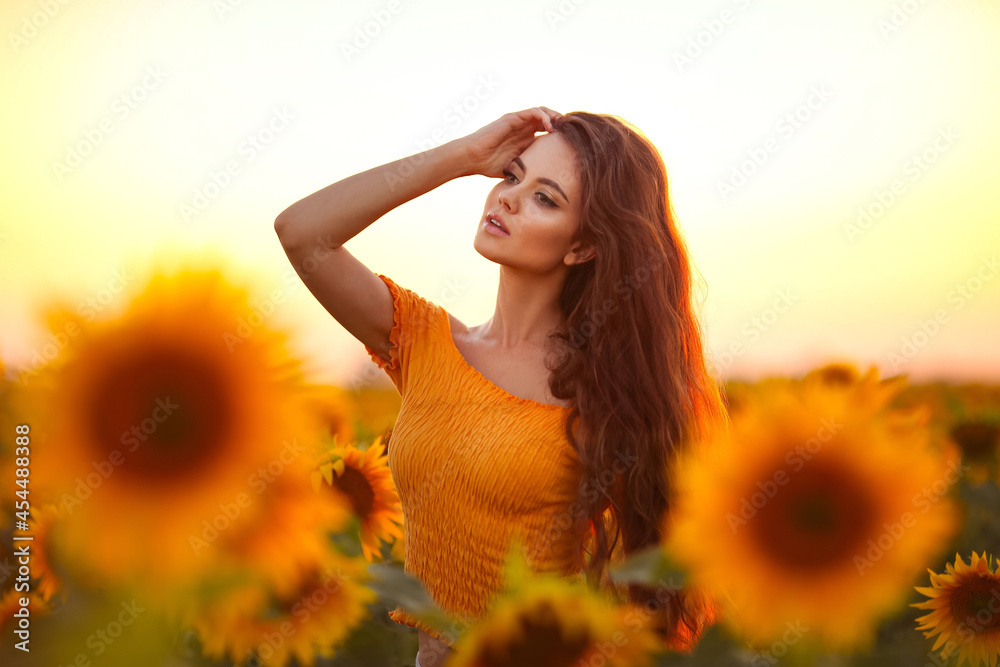 Beautiful young girl enjoying nature on the field of sunflowers at sunset. Summertime. Attractive brunette woman with long healthy hair. Beautiful young girl enjoying nature on the field of sunflowers at sunset. Summertime. Attractive brunette woman with long healthy hair.