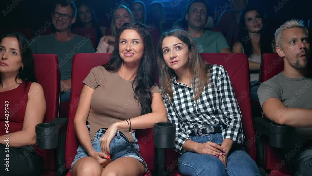 Two female friends gossiping discussing scene actors of film premiere sitting on armchair at cinema
