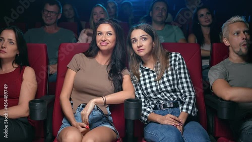 Two female friends gossiping discussing scene actors of film premiere sitting on armchair at cinema photo