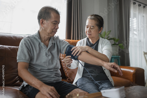 Asian senior couple checking blood pressure at home, a senior woman is helping her husband wearing an arm cuff of the blood pressure gauge.