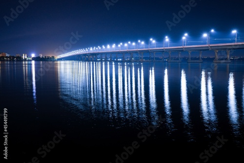 Reflection of bright lanterns in the Dnieper river under the bridge