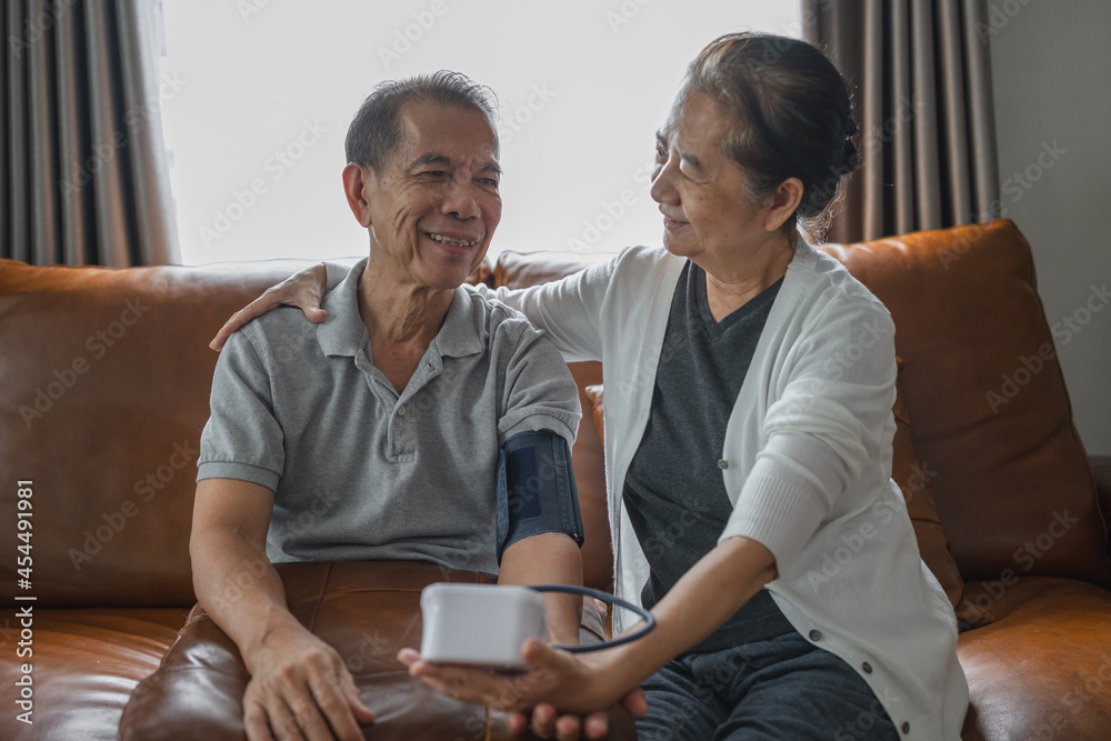 A close-up shot of an Asian senior couple checking blood pressure at home, after the blood pressure gauge shows the result they look at each other and smile. A close-up shot of an Asian senior couple checking blood pressure at home, after the blood pressure gauge shows the result they look at each other and smile.