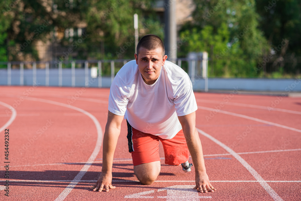 Caucasian male athlete with a prosthetic leg standing at the start on the track at the stadium. Sport concept.