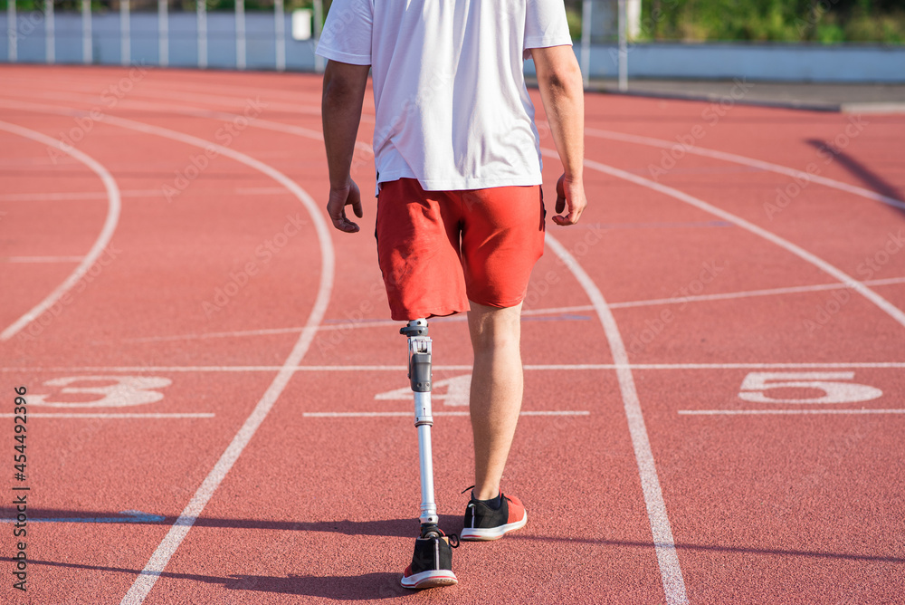 Caucasian male athlete with a prosthesis on his leg walking on the track at the stadium. Back view. Sport concept.