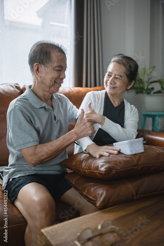 A close-up shot of an Asian senior couple checking blood pressure at home, after the blood pressure gauge shows the result they look at each other and smile with thumbs up. © Nawanon