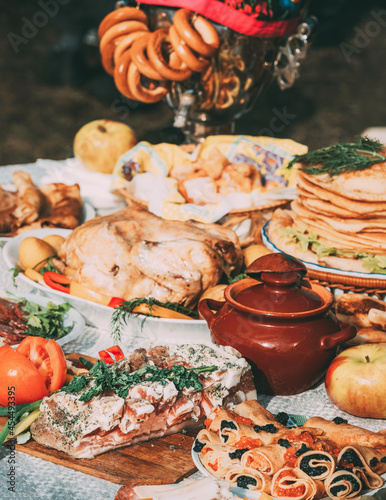 Dishes of the traditional Belarusian cuisine - pancakes, pancakes with caviar, lard, bacon, baked chicken, honey and samovar with steering wheels. Attribute of traditional folk celebration of