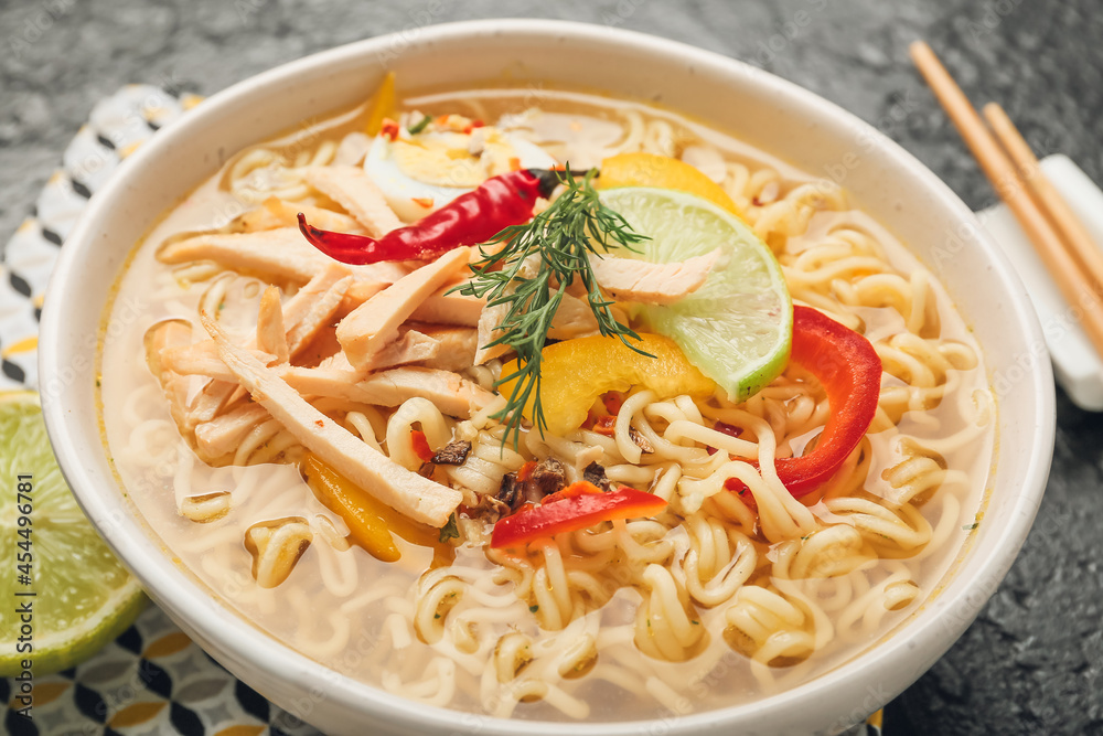 Bowl of tasty Thai soup with chicken on dark background, closeup